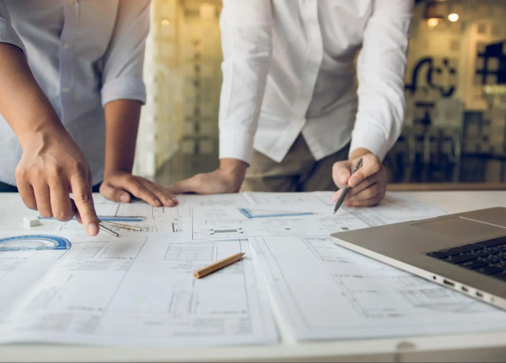 Two people working at a desk covered in paperwork.