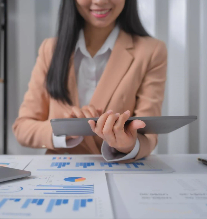 A woman sat at a desk covered in paperwork, working on a tablet computer.