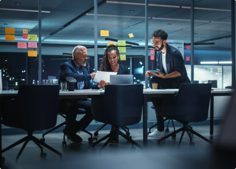 Three people work together around a large desk late at night.