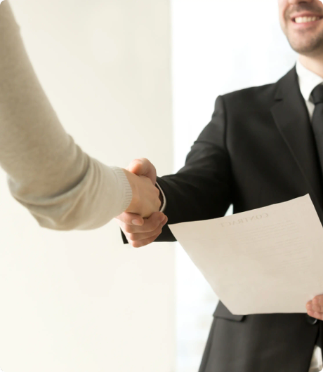 Two people shake hands, one of them is smiling and holding a piece of paper.