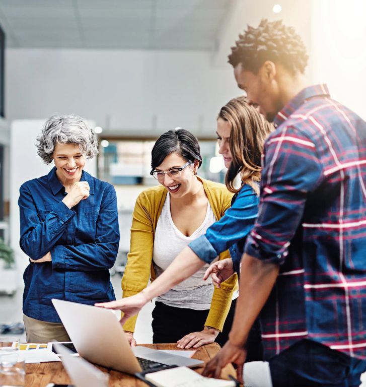 Four people standing at a desk looking at a laptop.