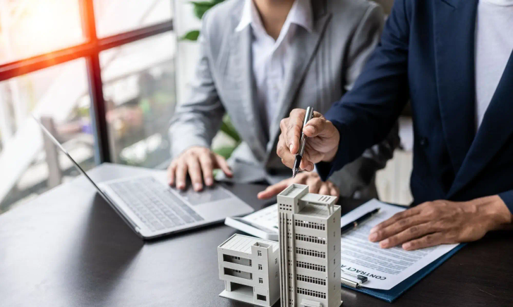 Two people work together at a desk with a model building and a laptop.