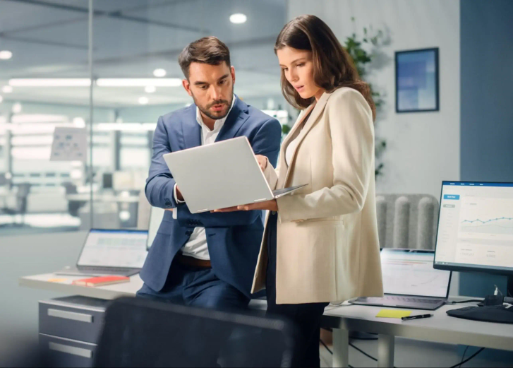 Two people are standing together looking at a laptop.