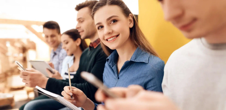 A group of people sat in a row writing on notepads or on phones.