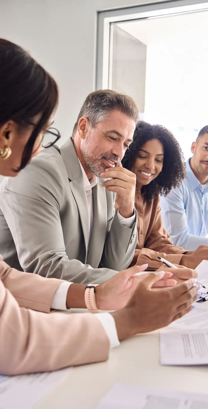 A group of people gathered around one side of a desk looking at documents.