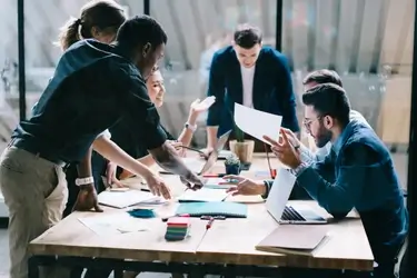 A group of people gather around a desk discussing the documents that are on it.